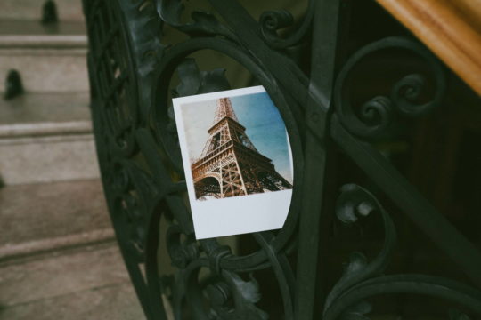 Ein Polaroidfoto vom Eiffelturm in Paris steckt in einem Treppengeländer.